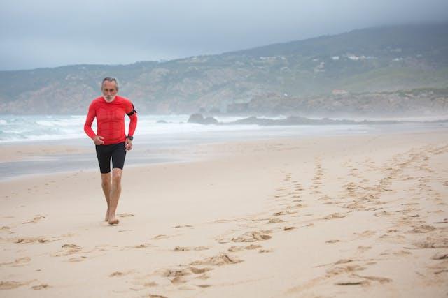 Homme senior avec haut rouge et cycliste noir qui court sur une plage